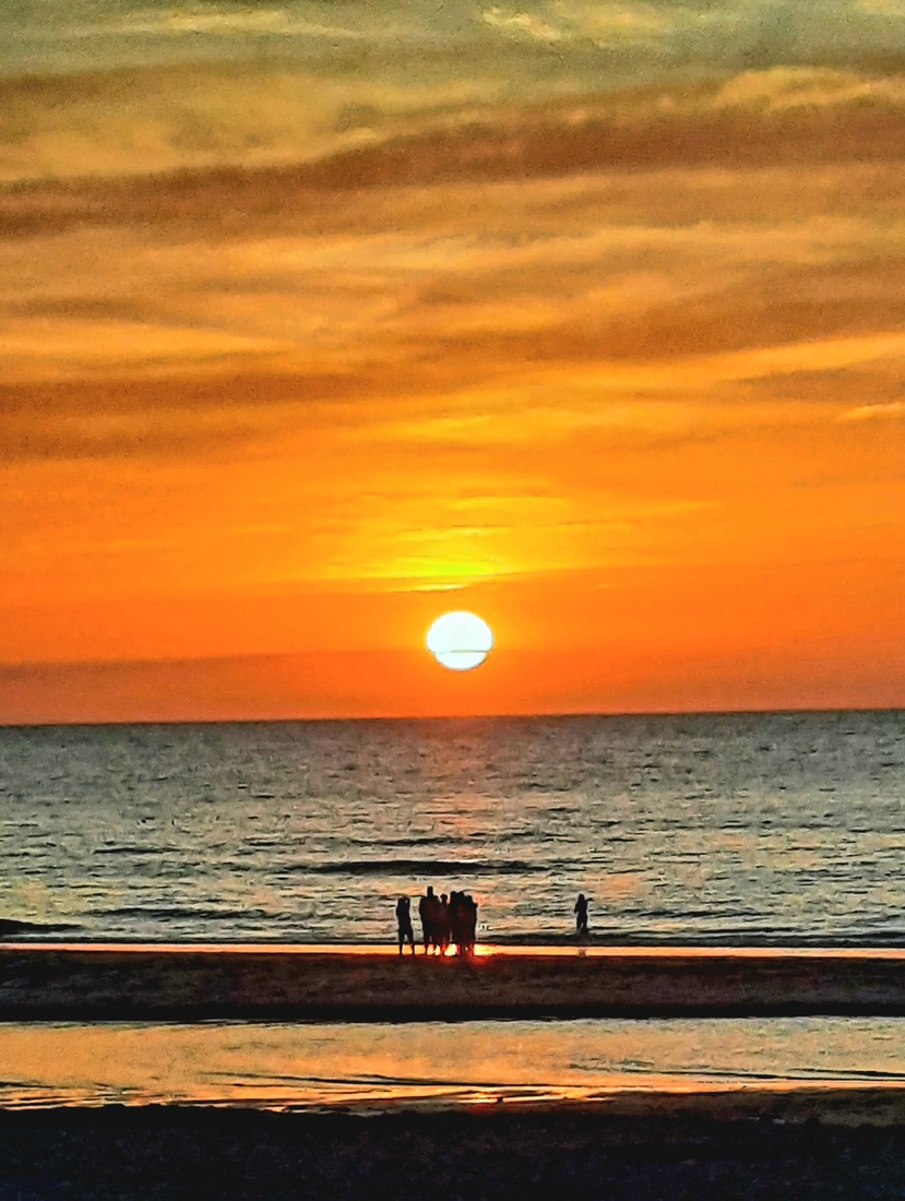 Mensen aan zee met ondergaande zon