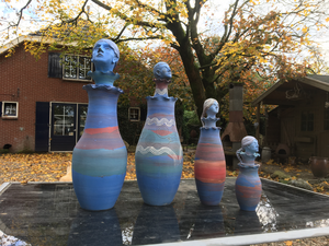 Dit zijn gedraaide vazen met een deksel met daarop een hoofd. De vormen zijn gedecoreerd met gekleurde klei-slibs (engobes), waarbij verschillende technieken zijn gebruikt (uitsparing, graveren etc.). Na droging zijn de vazen overgespoten met een zeer dunne laag transparant mat glazuur en daarna in één keer oxyderend of reducerend gestookt op 1080 tot 1100 graden.