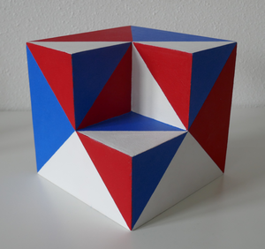 De kubus is 15 x 15 x 15 cm van 4 mm mdf. De uitsparing die naar binnen is 'geklapt', kan bestaan uit een vierkant, een kleine of grote driehoek. Doordat de vlakken van de gehele kubus in geometrische vormen geschilderd zijn, ontstaat er een optische illusie. Zowel de binnen- als buitenkant zijn geschilderd. De kubus kan op verschillende manieren uitgestald worden d.m.v. een bijgeleverde staander. Materiaal: mdf en acryl. Idee 1997 / uitvoering 2021.
In totaal zijn er 33 kubussen gemaakt.