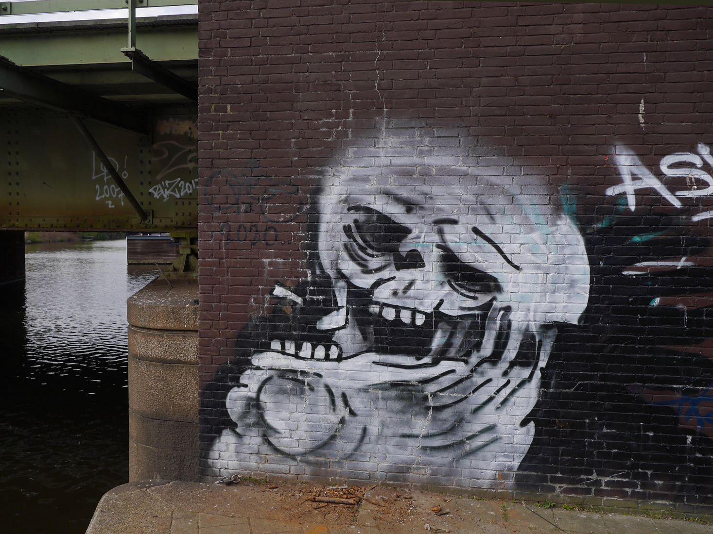 Grijnzende graffiti-face op de voet van de spoorbrug over de Nieuwe Vaart; foto Amsterdam / Mokum.
