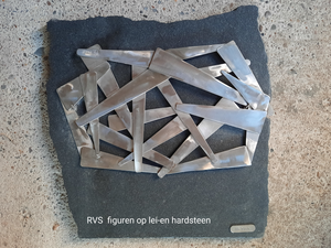 de roestvrijstalen figuren, abstract of figuratief, steken mooi af tegen een zwarte ondergrond en zijn een sieraad aan de wand.